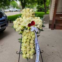 Cross-shaped floral spray of cream roses and white lilies with a ribbon