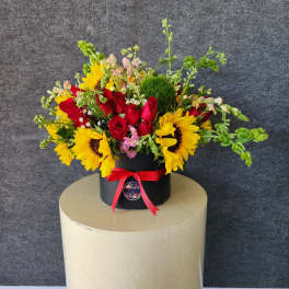 Bouquet of red roses and yellow sunflowers in a black box with a red ribbon