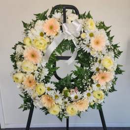 Round floral wreath with white and pale peach flowers on a black stand