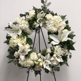 White floral wreath on a black stand with lilies, roses, and hydrangeas
