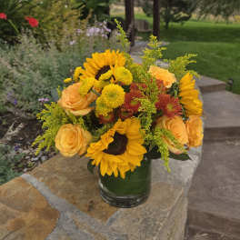 Bouquet of sunflowers, yellow roses, and mums in a glass vase