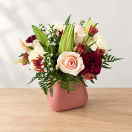 Mixed bouquet of roses, carnations, and lilies in a pink vase