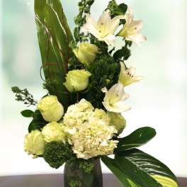 White lilies and pale green flowers in a glass vase