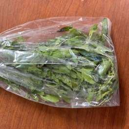 Plastic-wrapped bunch of green leafy stems on a wooden surface