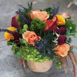 Mixed bouquet with peach roses, burgundy calla lilies, and yellow blooms in a burlap pot