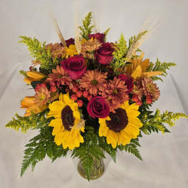 Bouquet of sunflowers, roses, and mums in a clear glass vase
