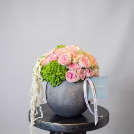 Pink roses and green hydrangea in a dark round vase with trailing white flowers