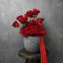 Red roses arranged in a gray vase with a red hanging ribbon