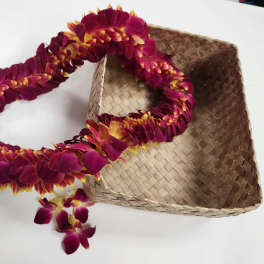 Magenta and yellow flower lei beside a woven straw hat