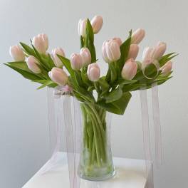 Arrangement of pale pink tulips in a clear glass vase with long sheer pink ribbons