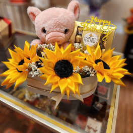Pink plush pig in a box with yellow sunflowers and chocolates
