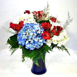 Bouquet of red roses, blue hydrangeas, and white flowers in a blue vase