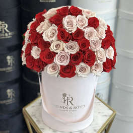 Red and blush roses arranged in a round pink hat box