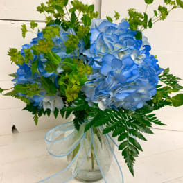 Blue hydrangea bouquet in a glass vase with a light blue ribbon