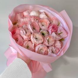 Handheld bouquet of pale pink ranunculus wrapped in pink paper