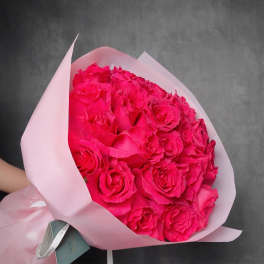 Large bouquet of hot pink roses wrapped in pale pink paper against a dark background