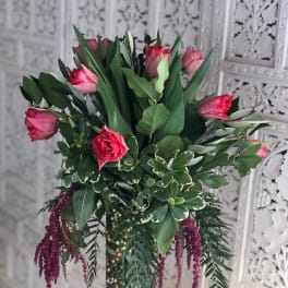 Pink tulips in a clear glass vase with mixed greenery