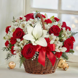 Basket arrangement of red roses, white lilies, and red carnations with a red ribbon
