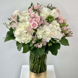 Pink and white bouquet in a clear glass vase with a gold base