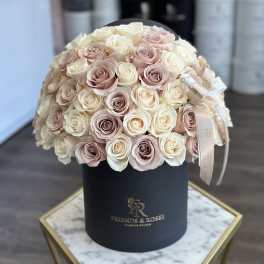 Round bouquet of blush and ivory roses in a black hat box.