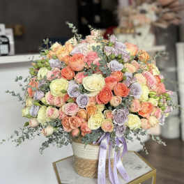 Large bouquet of pastel roses in a woven basket with a lavender ribbon