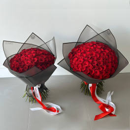 Two large bouquets of red roses wrapped in black translucent paper with long red and white ribbons.