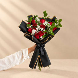 Handheld bouquet of red roses with white filler flowers in black wrap