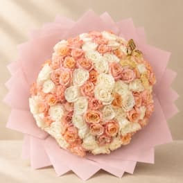 Round bouquet of peach and white roses wrapped in pink paper