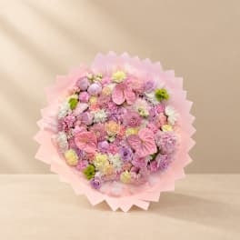 Round bouquet of pink and lavender flowers wrapped in pale pink paper