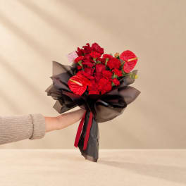 Red flower bouquet wrapped in dark paper with a ribbon