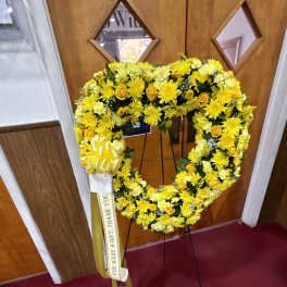 Yellow floral wreath on a stand with a ribbon and bow
