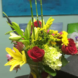 Mixed bouquet of roses, lilies, hydrangea, and daisies in a glass vase