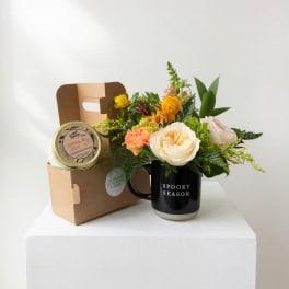 Flower arrangement in a black mug with a candle gift box beside it