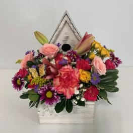 Mixed bouquet in a white birdhouse container with a butterfly accent
