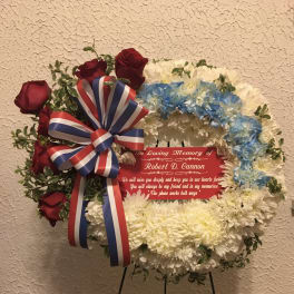 Memorial wreath with red roses, white and blue flowers, and a ribbon on a stand
