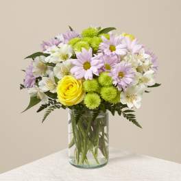 Pink daisies, white alstroemeria, and yellow roses in a glass vase.