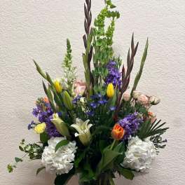 Tall mixed bouquet in a clear glass vase with white, purple, yellow, and orange blooms