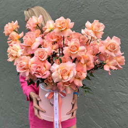 Pink roses arranged in a round hatbox with a ribbon bow