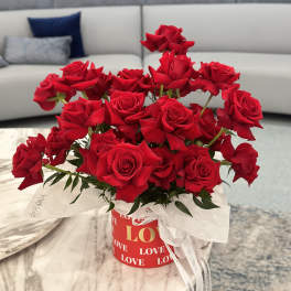 Red roses arranged in a round gift box with a white ribbon.