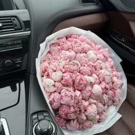 Large bouquet of pink peonies wrapped in white paper on a car seat
