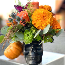 Orange and coral flowers arranged in a black skull vase