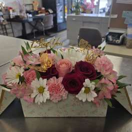 Pink and white flower arrangement in a floral box with gold toppers