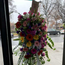 Tall standing spray of mixed pink, white, purple, and yellow flowers with ribbon