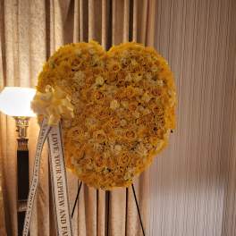Heart-shaped yellow floral standing spray on an easel with a memorial ribbon