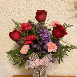 Bouquet of red roses, purple flowers, and pink carnations in a glass vase with a ribbon