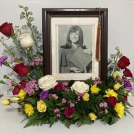 Sympathy floral arrangement around a framed portrait with red, white, and yellow flowers