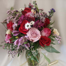 Mixed bouquet of roses, daisies, and purple blooms in a glass vase