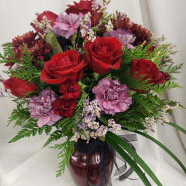 Bouquet of red roses and purple carnations in a burgundy vase