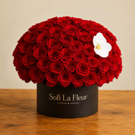 Round arrangement of red roses in a black box with a white orchid accent