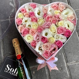 Heart-shaped box of pink and white roses with a champagne bottle and gift bag